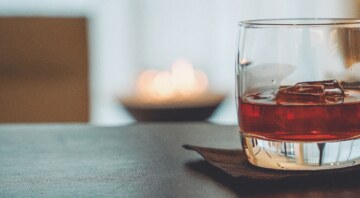 A drink with ice cubes in front of a blurred background with candlelight.