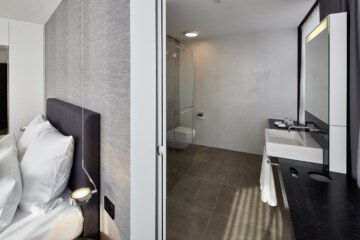 View of the minimalist bedroom and bathroom area in one of the double rooms of the modern hotel room in Munich.