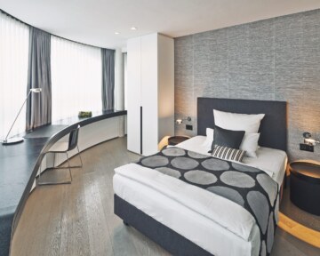 Modern single hotel room in Munich with comfortable bed, side table and desk.