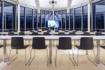 Der Konferenzraum "Ellipse 1" in der Tagungslocation bei München mit großen Fenstern und Bildschirm.