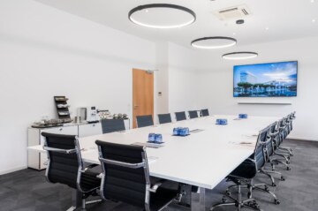 Konferenzraum "Kubus" in der Tagungslocation bei München mit länglichem Tisch, Bildschirm und Snacks.